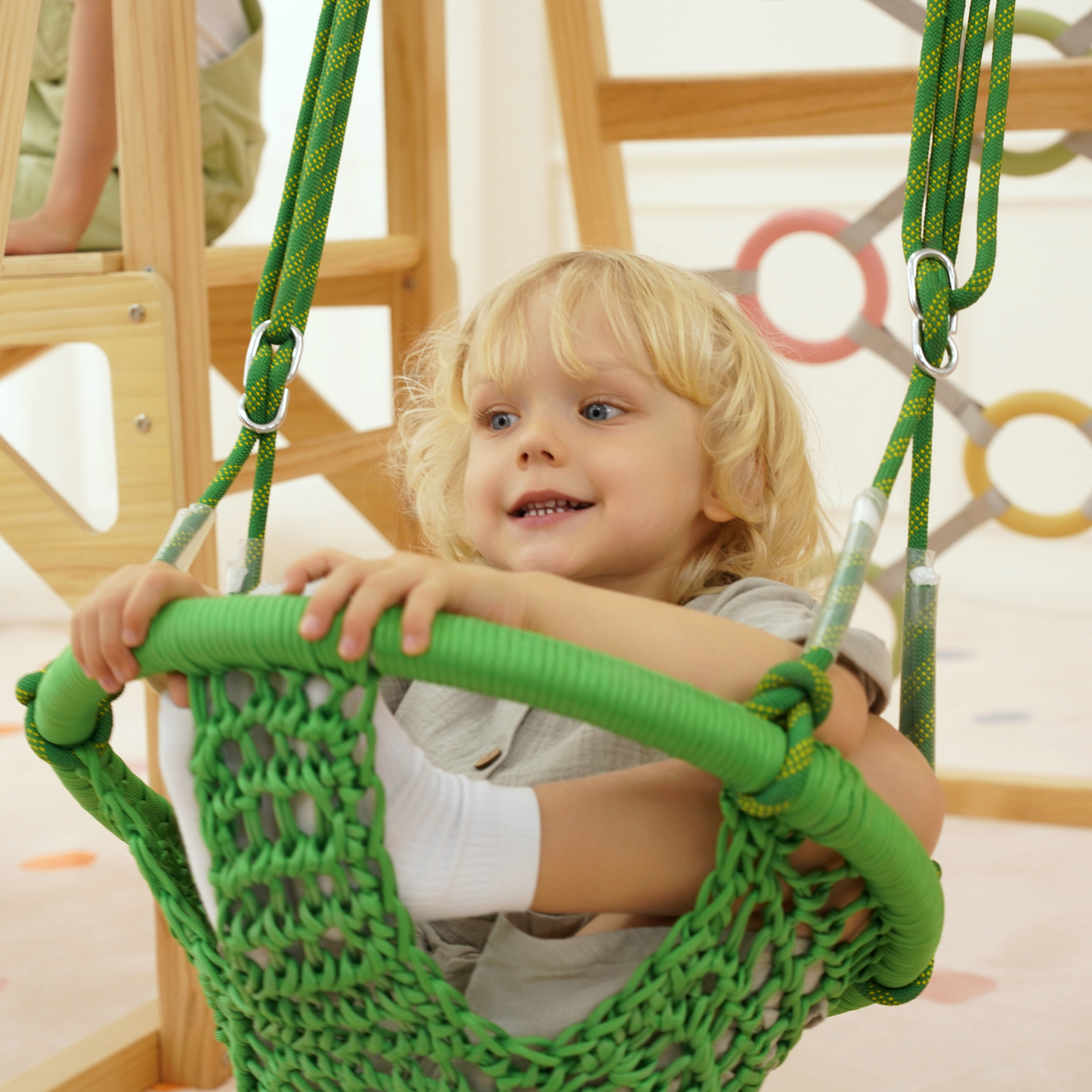 Smiling child sitting in green sensory swing attached to Montessori wooden climber