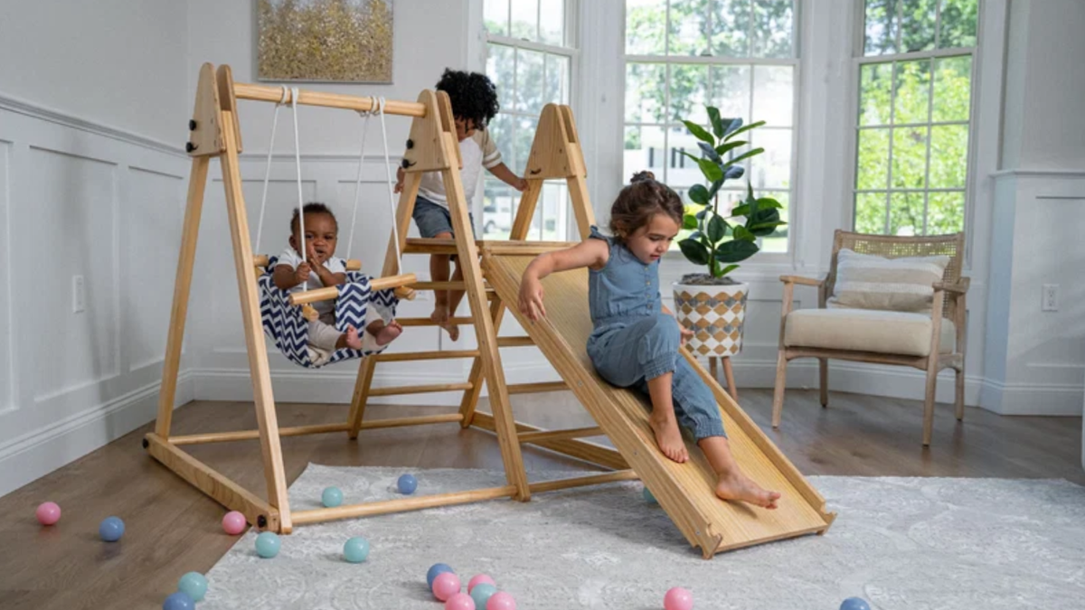 Toddler sliding down a wooden indoor jungle gym in a family living room