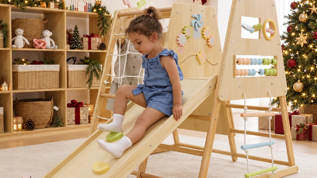 Toddler sliding down an Avenlur wooden indoor climber with sensory activity panels and a rope ladder, beside a decorated Christmas tree