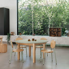 Modern dining area with wooden tables and chairs near a large window with greenery outside.
