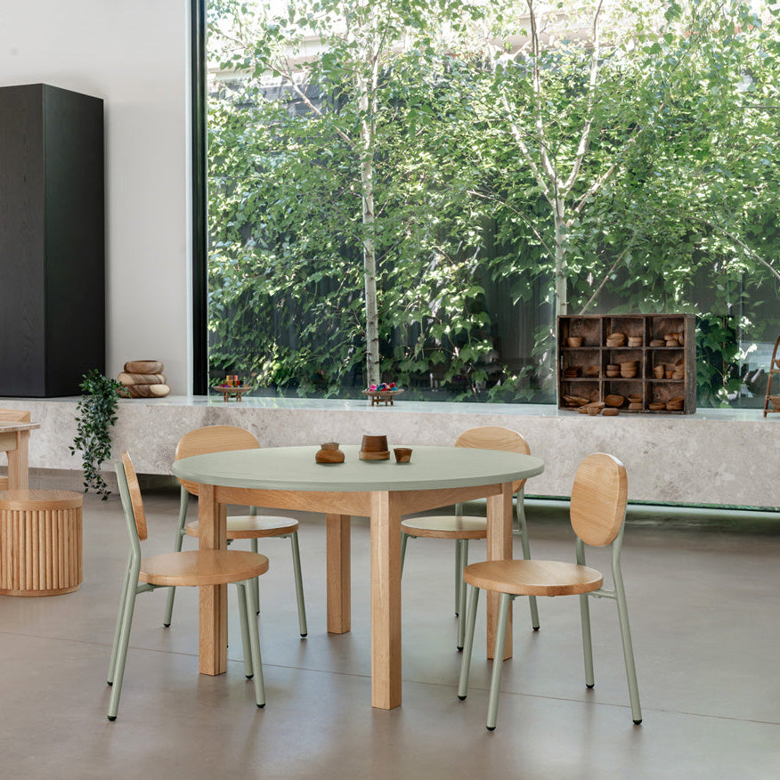 Modern dining area with wooden tables and chairs near a large window with greenery outside.