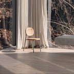 Wooden chair in front of a large window with white curtains and a view of trees.