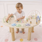 Child playing with a wooden activity table filled with colorful toys on a white floor.