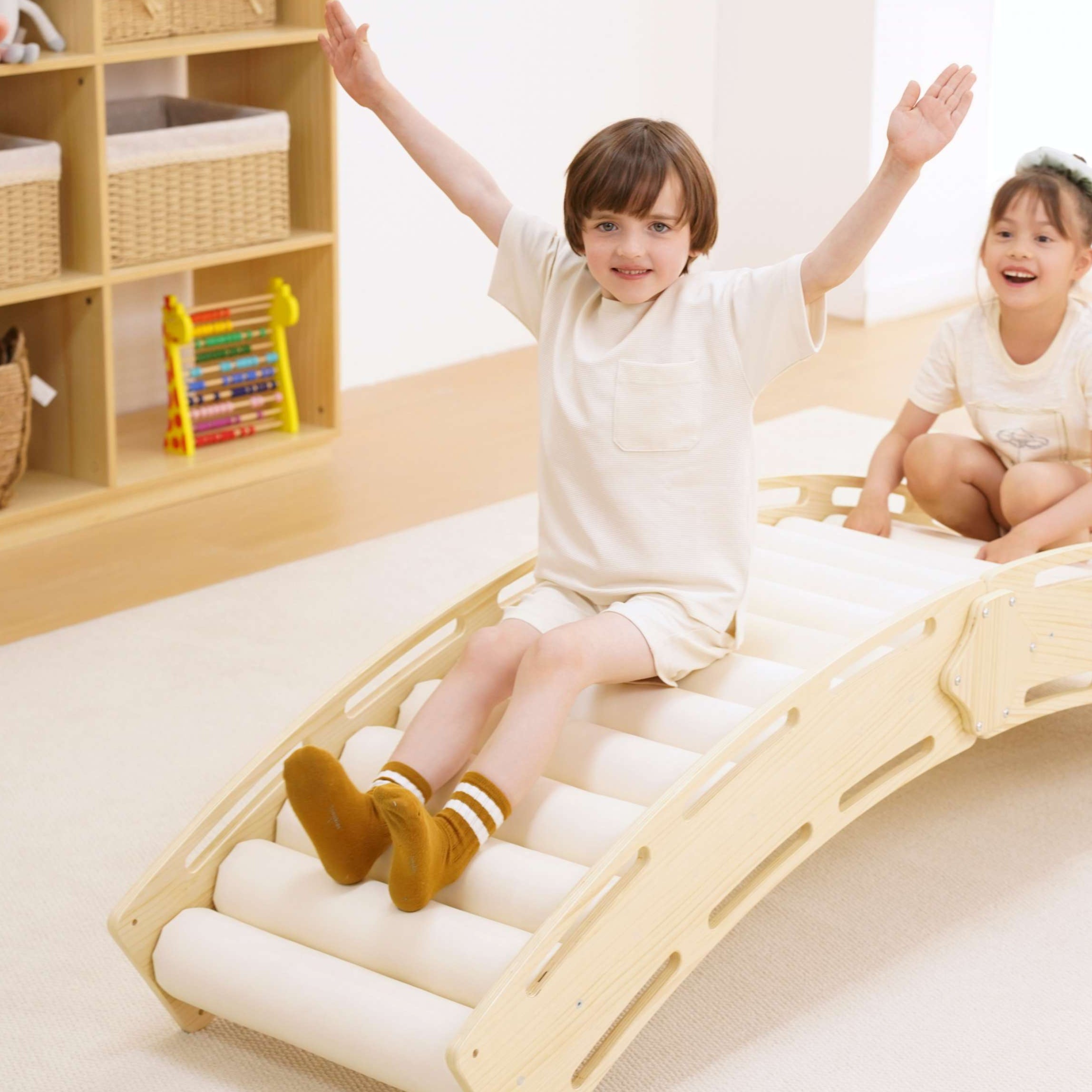 Two children playing on a wooden wave-shaped bed in a room with shelves and toys.