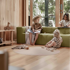 Children playing in a modern living room with green sofa and wooden floor.