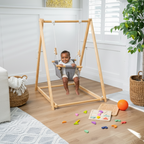 Child playing on a wooden swing set in a bright, well-lit room with toys scattered on the floor.


