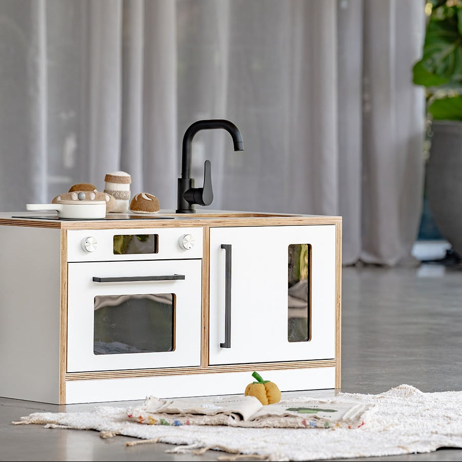 Children's play kitchen set with white cabinets and black fixtures on a light wooden surface.