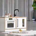 Children's play kitchen set with white cabinets and black fixtures on a light wooden surface.