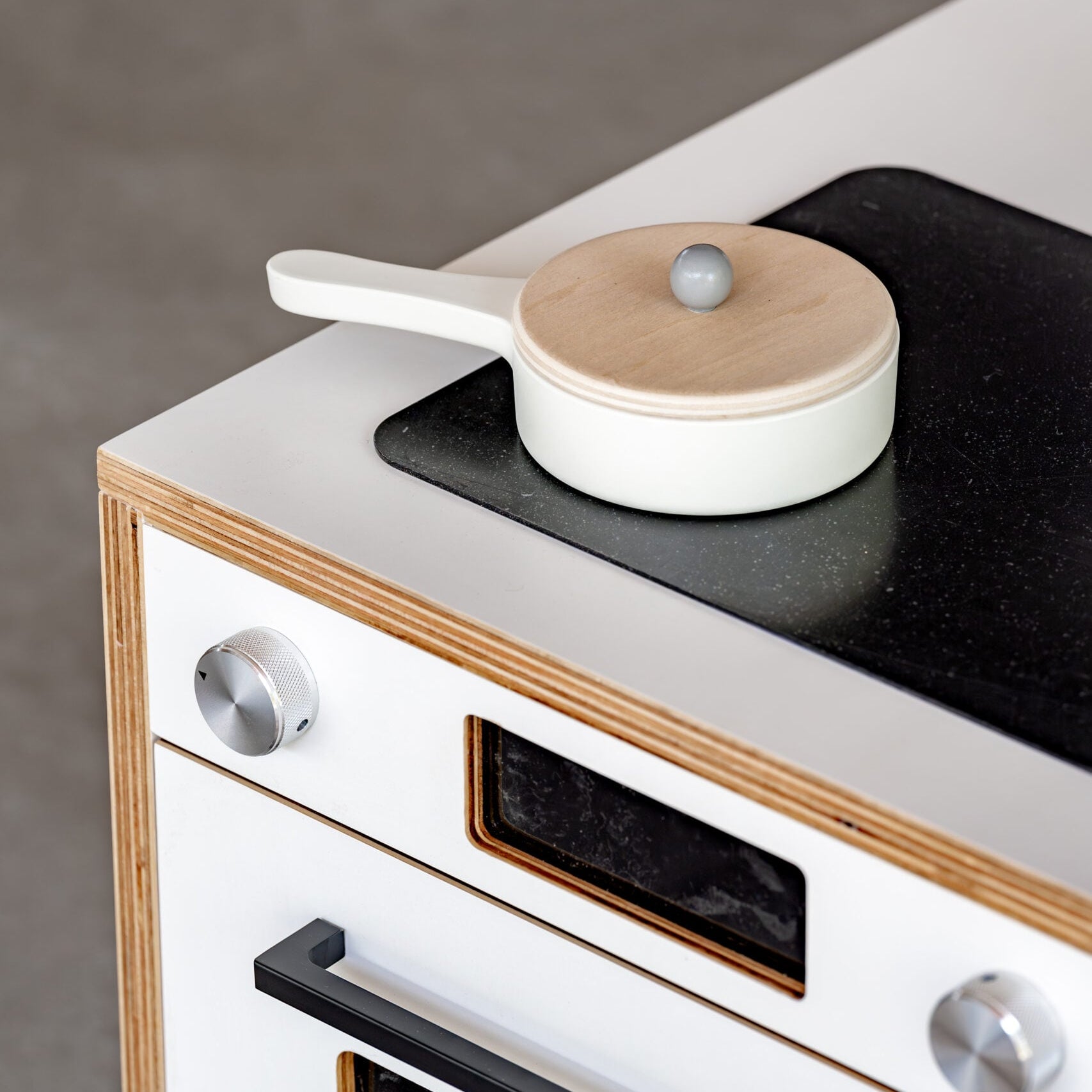 White stove with black cooktop and wooden accents, featuring a small white pot with a wooden lid.