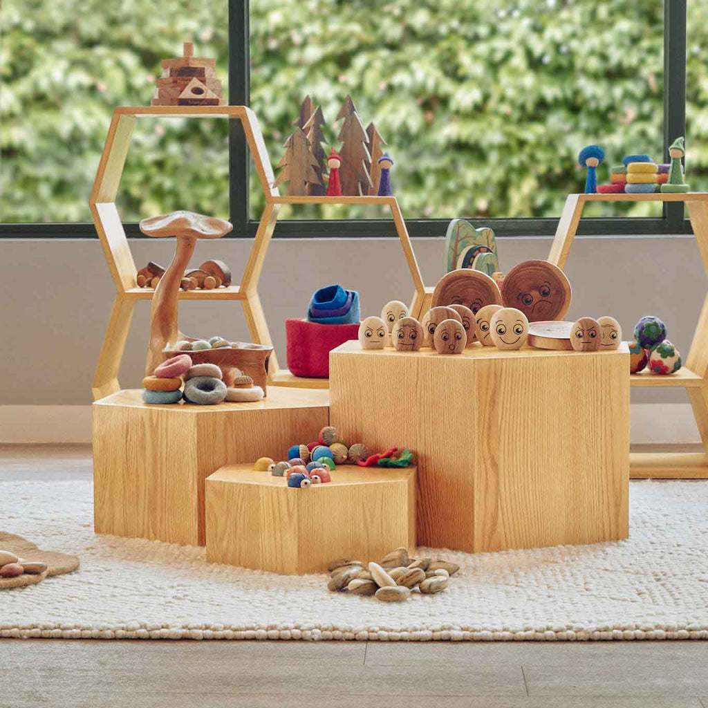 Wooden toy set with various toys on a wooden platform in a room with large windows.