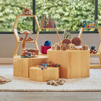 Wooden toy set with various toys on a wooden platform in a room with large windows.