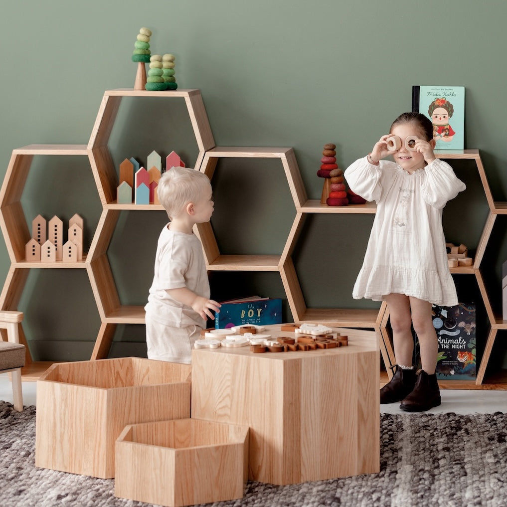 Children playing in a room with wooden shelves and furniture.