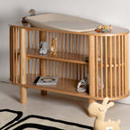 Wooden baby changing table with shelves and toys on a light background
