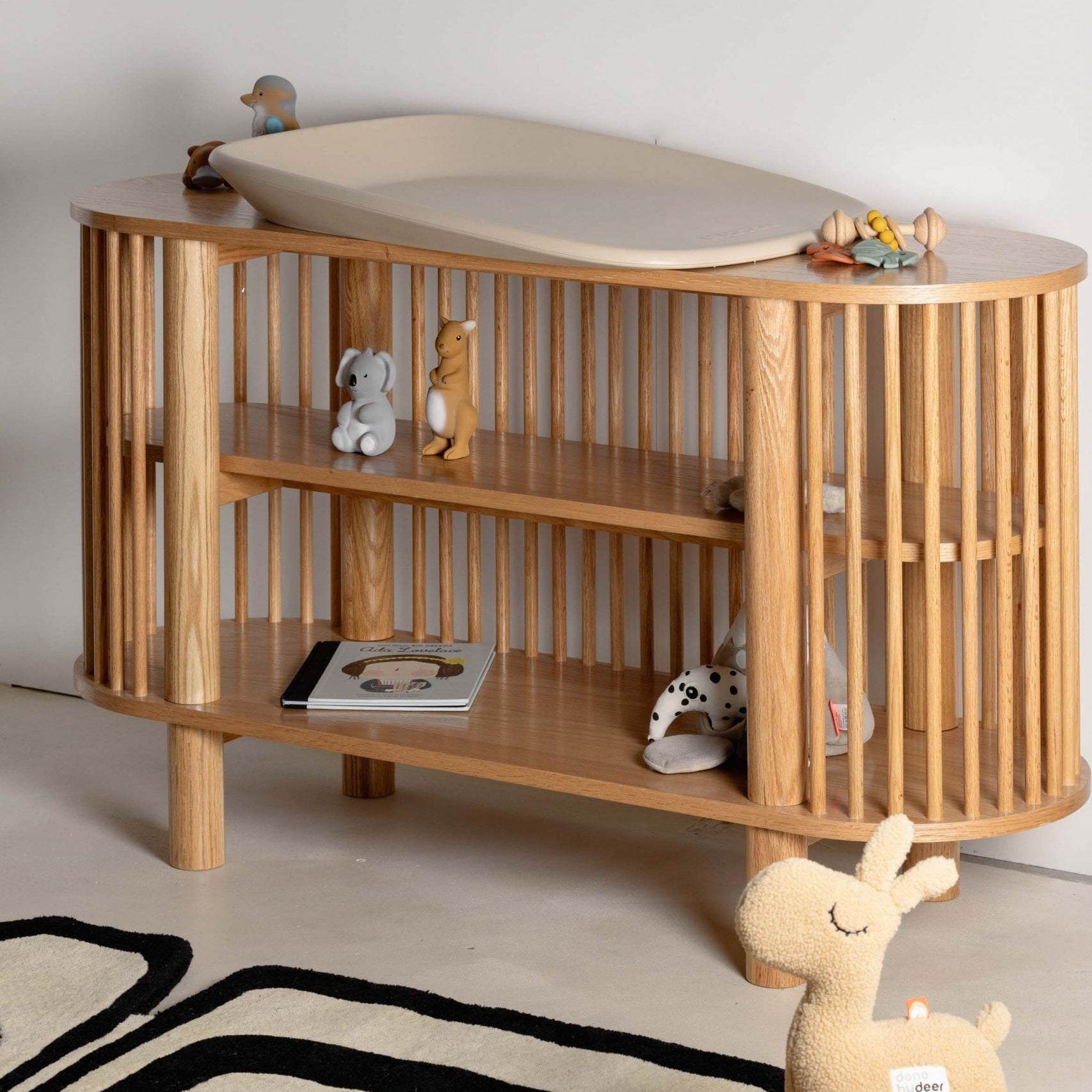 Wooden baby changing table with shelves and toys on a light background