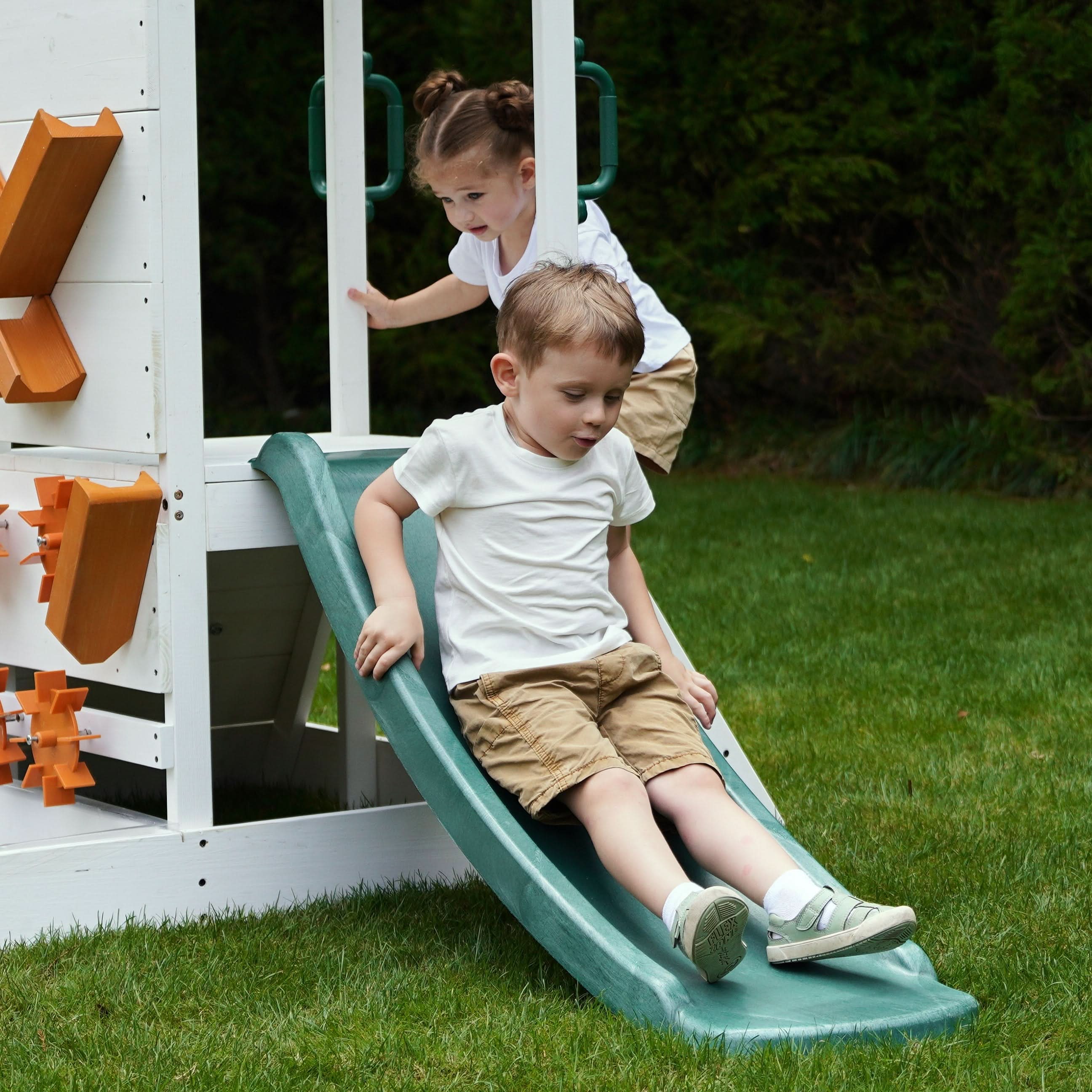 Kids sliding down the Avenlur Aloe outdoor playhouse slide in backyard