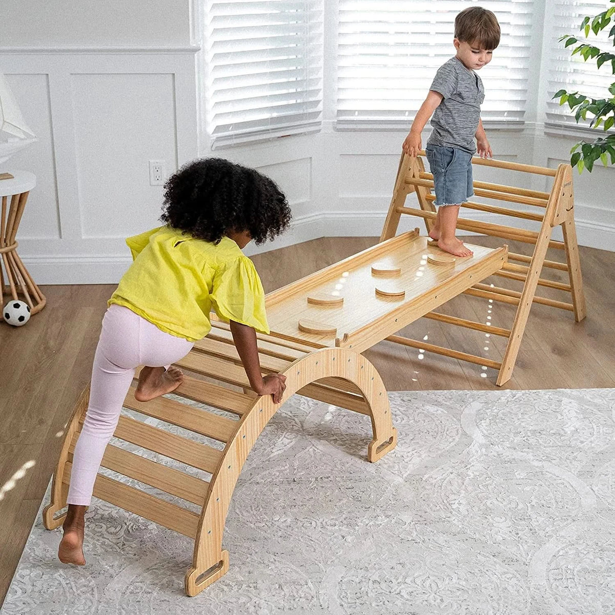 Two toddlers climbing on an Avenlur Pikler triangle set with rocker and slide in a bright playroom