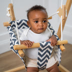 Baby sitting in the Avenlur navy and white chevron cotton baby swing seat, holding the wooden front bar