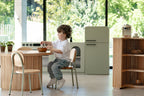 Child playing in a Montessori kitchen with the sage green fluted fridge nearby