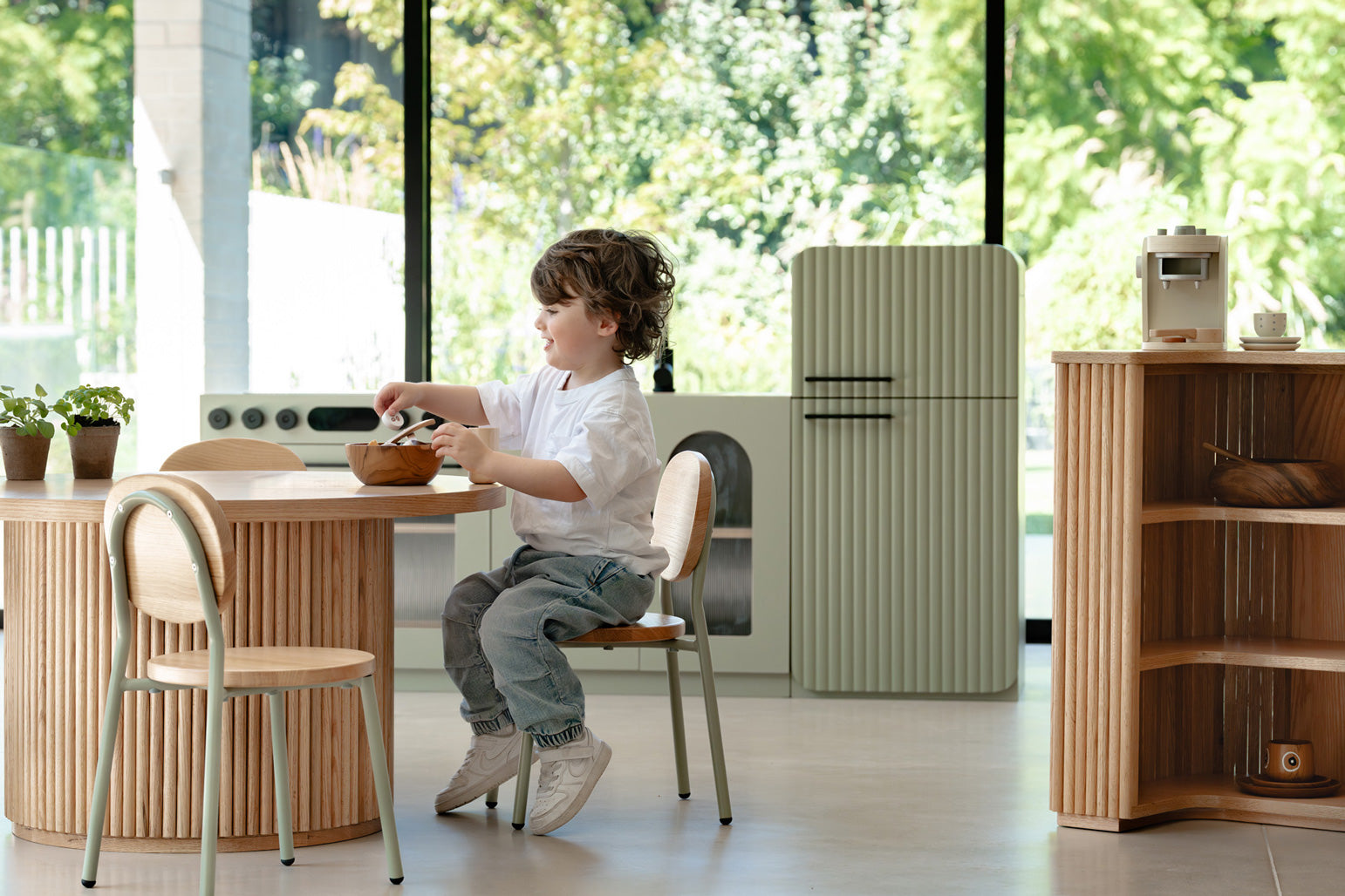 Child playing in a Montessori kitchen with the sage green fluted fridge nearby