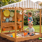 Children playing in a wooden sandbox with a striped roof in a garden setting.