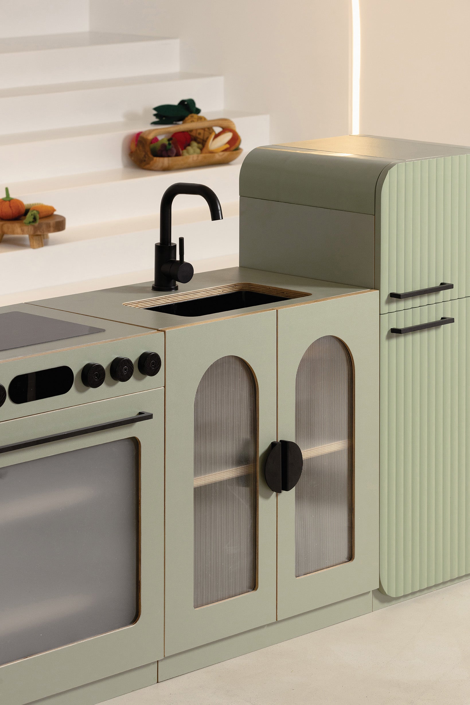 Close-up of the sage green fluted sink with black faucet beside the oven and fridge