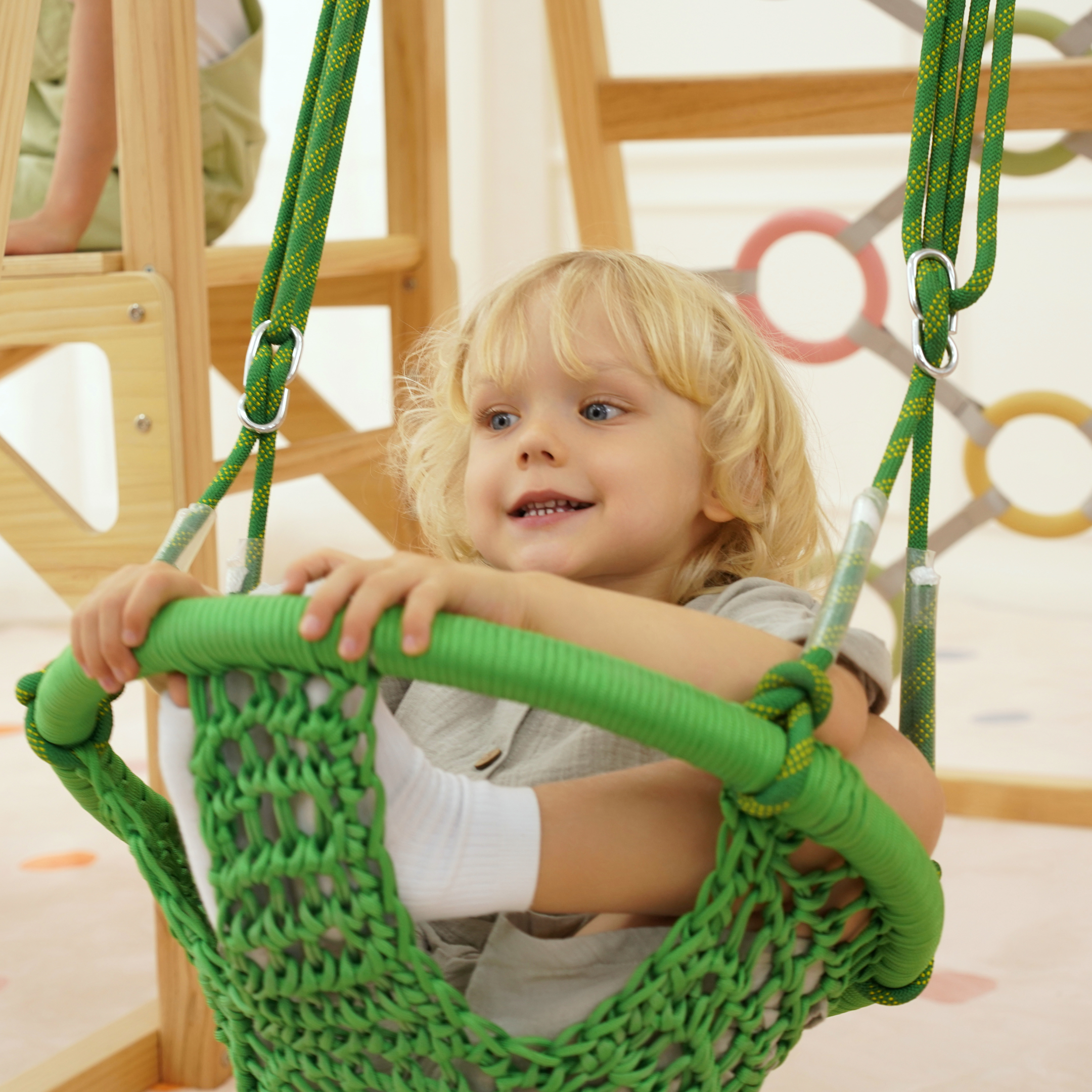 Smiling child sitting in green sensory swing attached to Montessori wooden climber