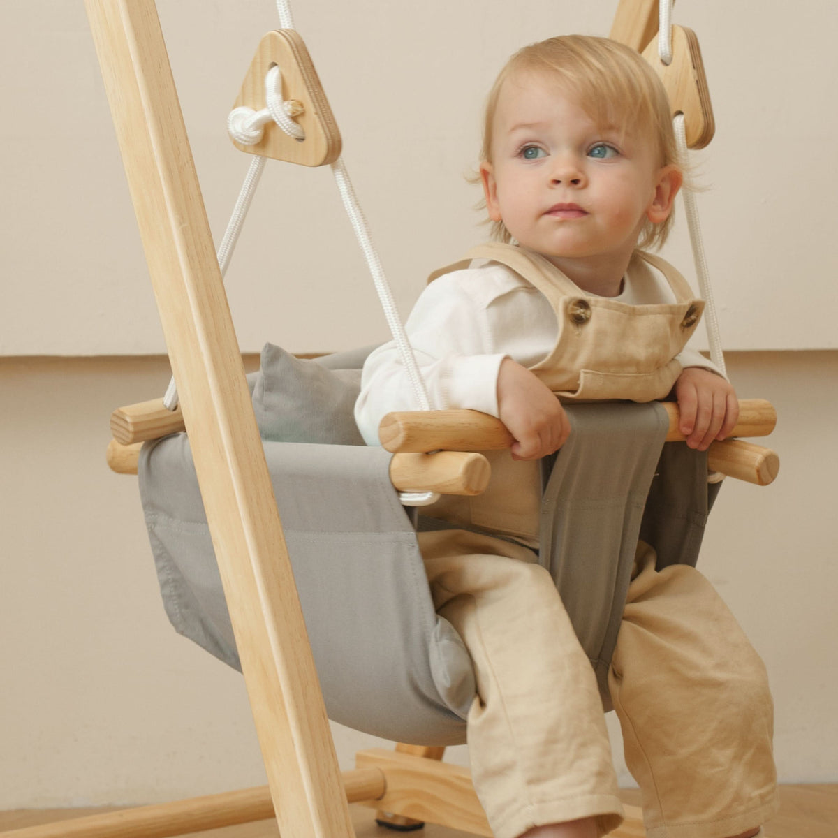 Toddler sitting in the Avenlur gray cotton canvas hammock swing seat hanging from a wooden swing stand