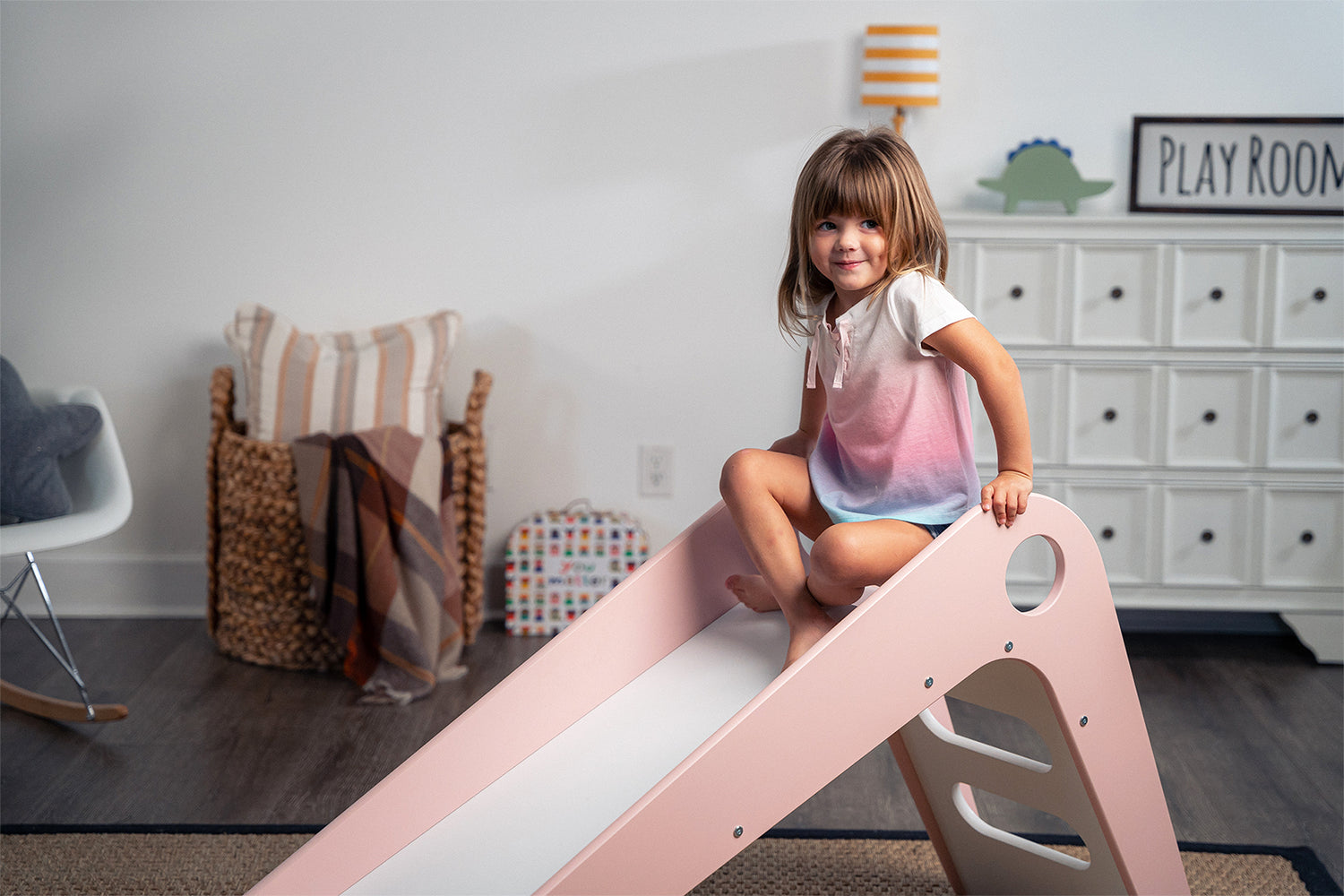 Adorable Girl Sitting on Top of Manuka - Avenlur's Safe and Fun Indoor Toddler Slide in Playroom. Shown in Pink.