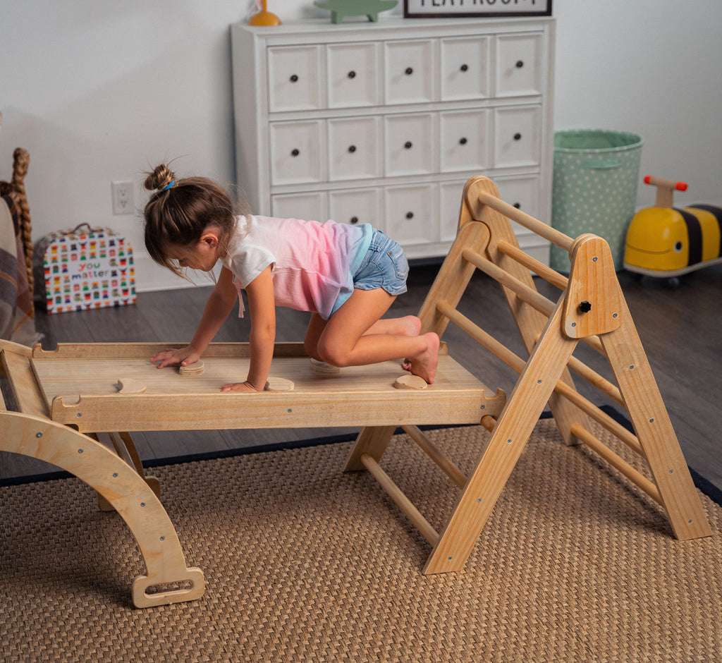 Young girl crawling across Avenlur Hazel Pikler Triangle slide bridge in cozy playroom
